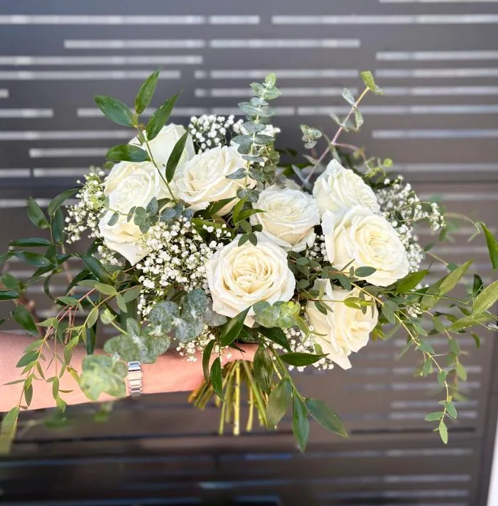 Classic bridal bouquet by DeVine's: white roses, baby's breath and eucalyptus, held in hand